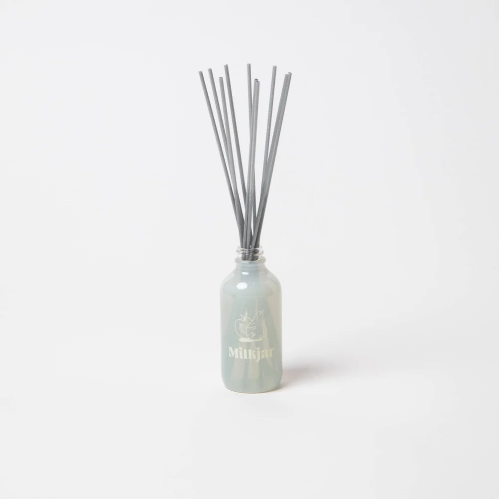 A sleek translucent light blue glass reed diffuser bottle with gray reeds for pear and nectarine diffuser smells