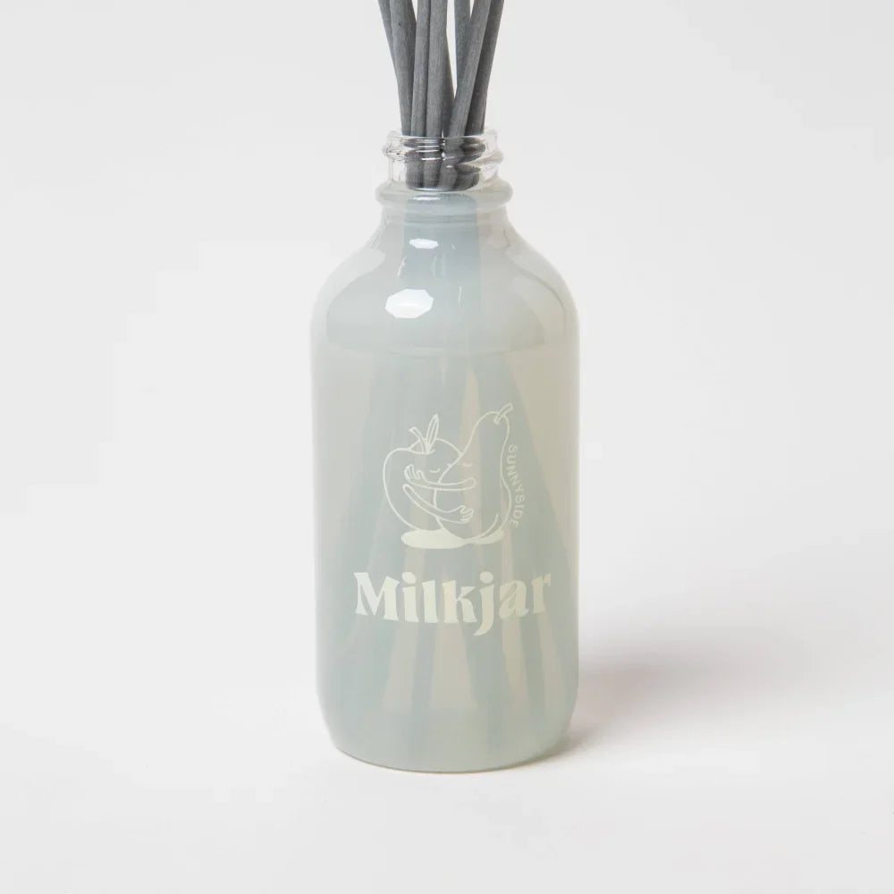 A translucent gray frosted glass milkjar reed diffuser with an etched logo for sunnyside pear and nectarine diffuser smells