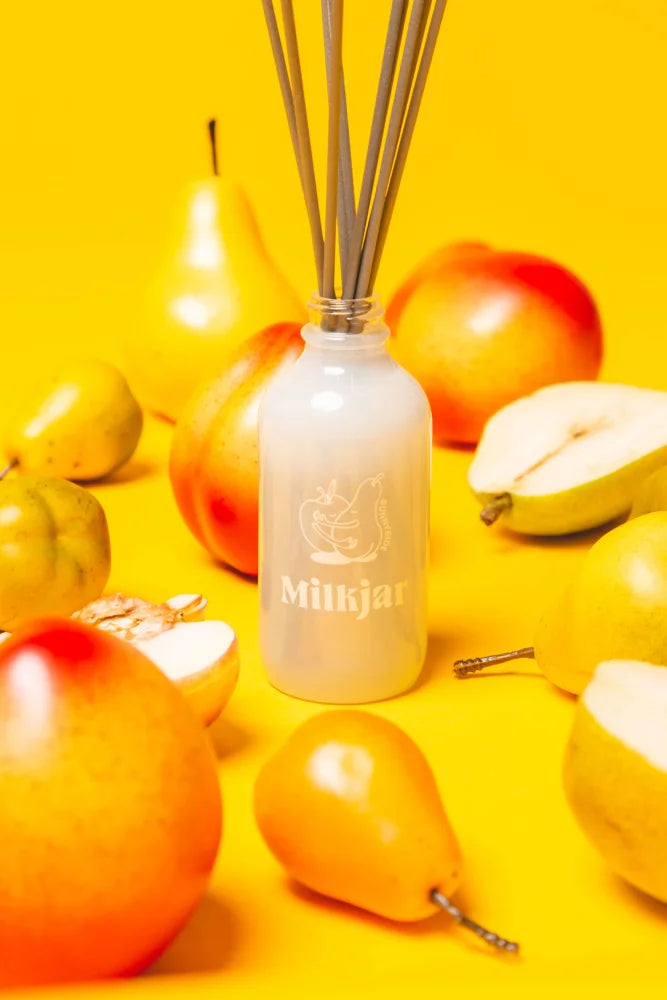 A frosted white glass reed diffuser bottle with metal reeds and milkjar logo featuring pear and nectarine diffuser smells
