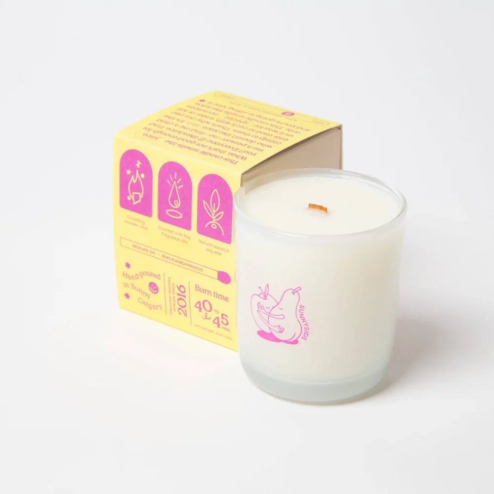 A white coconut soy candle in a clear jar with a pink pear design from sunny side that smells like pear and nectarine