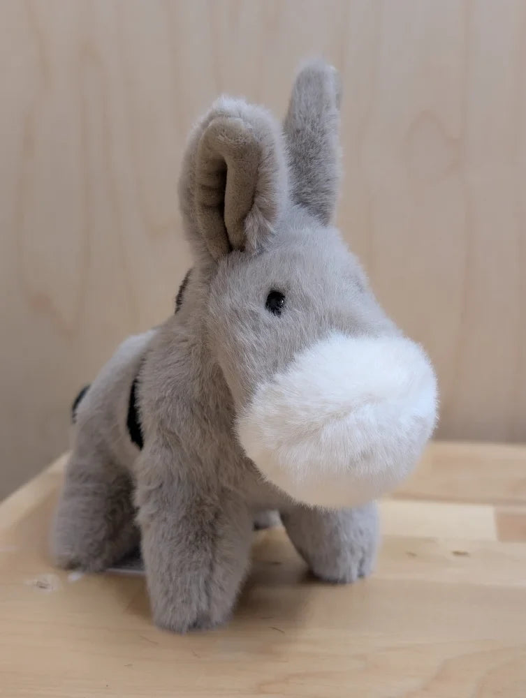 The donkey soft gray plush donkey with white muzzle and black eyes standing on a wooden surface