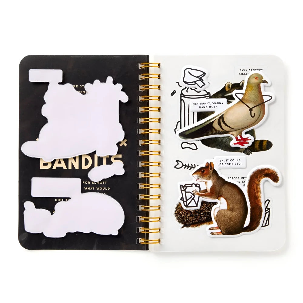 Gold spiral notebook open to black and white trash bandits sticker page with pigeon raccoon and squirrel designs