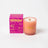 A peach-colored wallflower tobacco and peony coconut soy candle in frosted glass with gold lettering and wooden wick