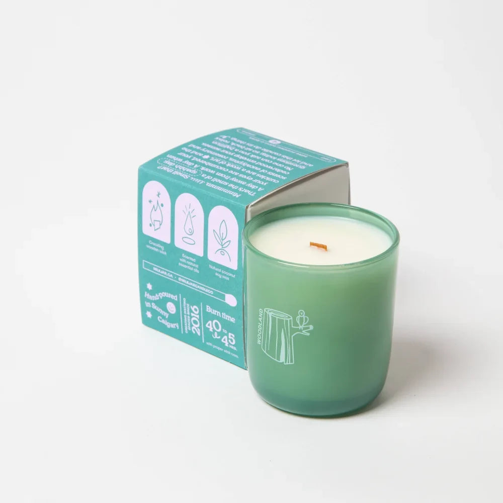 Woodland essential oil coconut soy candle in translucent green glass with white wax and orange wick featuring tree stump design