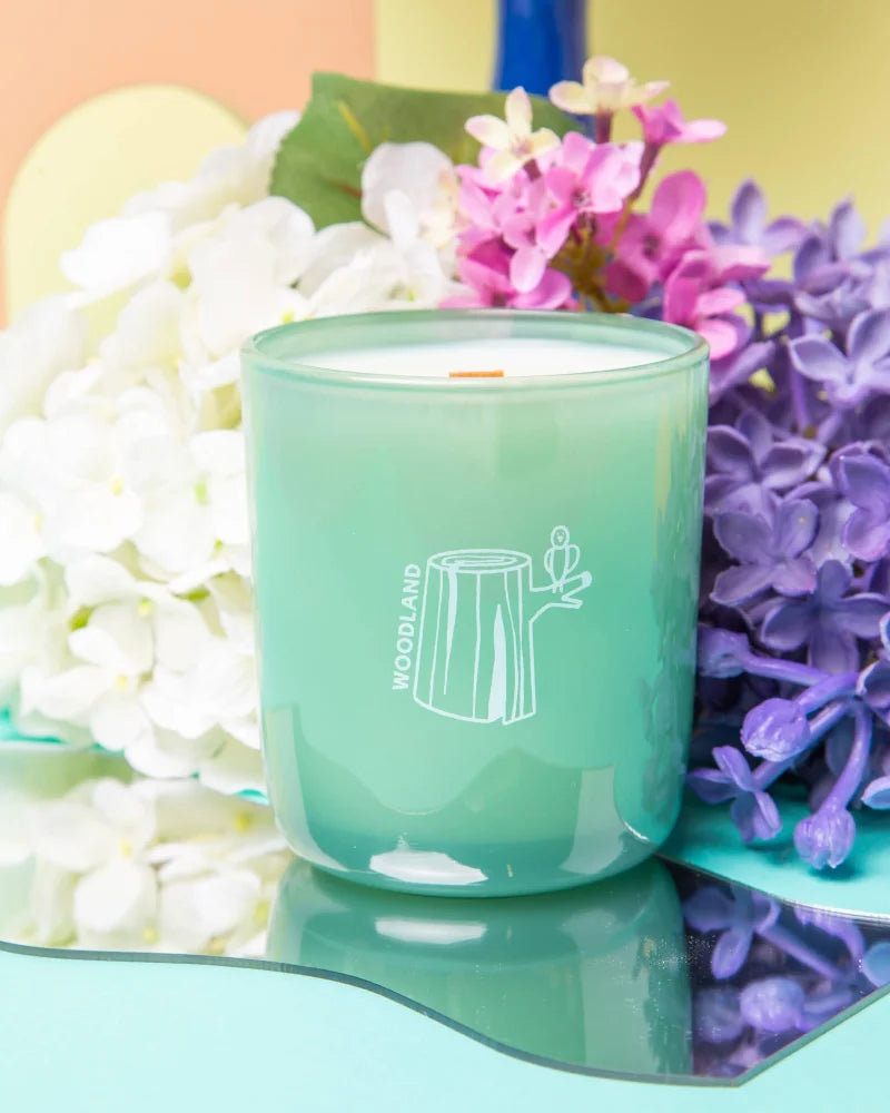 A mint green glass candle jar with white tree stump design and woodland label for essential oil coconut soy candle