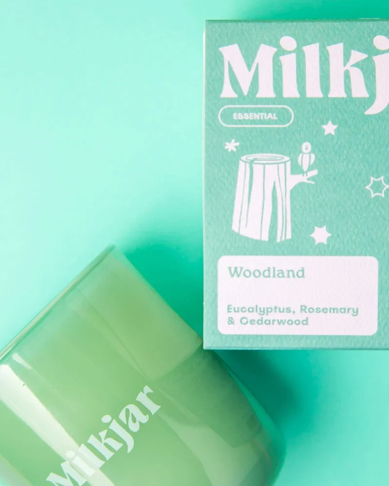 A translucent green glass essential oil candle jar with coconut soy wax by milkjar beside mint-green woodland packaging