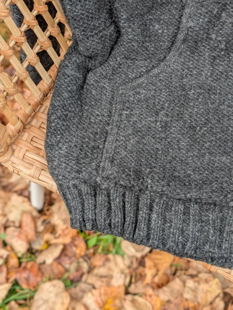 A cozy dark gray calgary cardigan in zealand wool with cable knit texture and ribbed cuffs, no attached hood visible