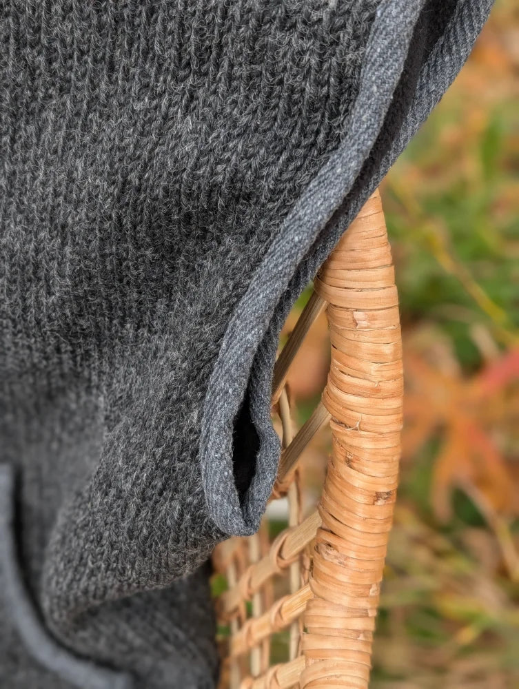 A dark gray woolen jasper vest with soft fleece texture draped over a woven wicker chair highlighting zealand wool quality