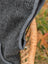 A dark gray woolen jasper vest with soft fleece texture draped over a woven wicker chair highlighting zealand wool quality